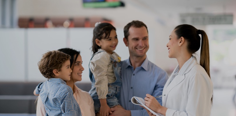 Χαμογελαστοί γονείς κρατούν αγκαλιά τα παιδιά τους και συζητούν με τη γιατρό τους.