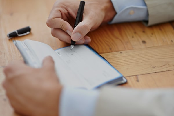 Ανδρικό χέρι συμπληρώνει ποσό σε μπλοκ επιταγών.